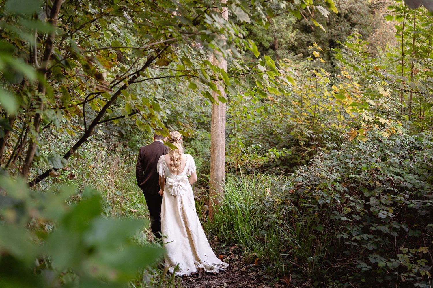 Bride and groom share a romantic moment on a forest path surrounded by lush green trees and foliage.