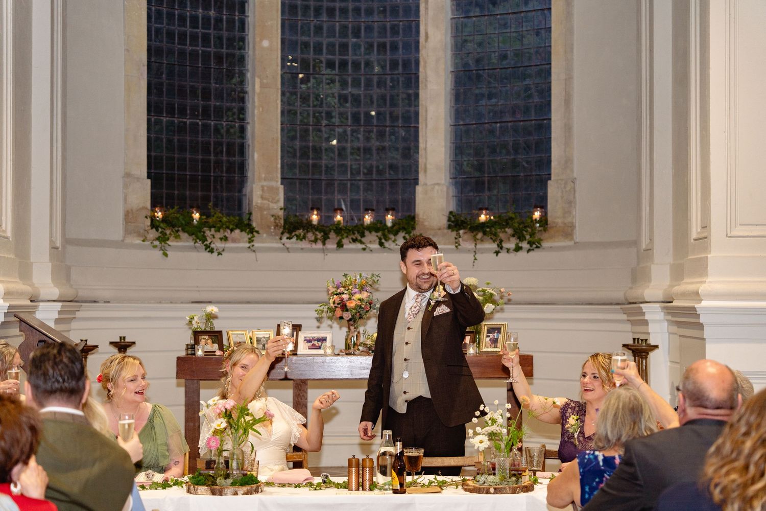 Groom raises a champagne toast surrounded by wedding guests at a stunning church reception venue.