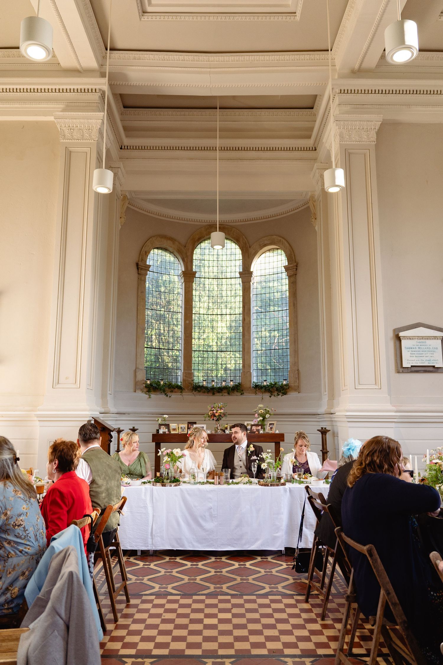 Elegant wedding reception inside historic church with arched stained glass windows and guests seated at decorated tables.
