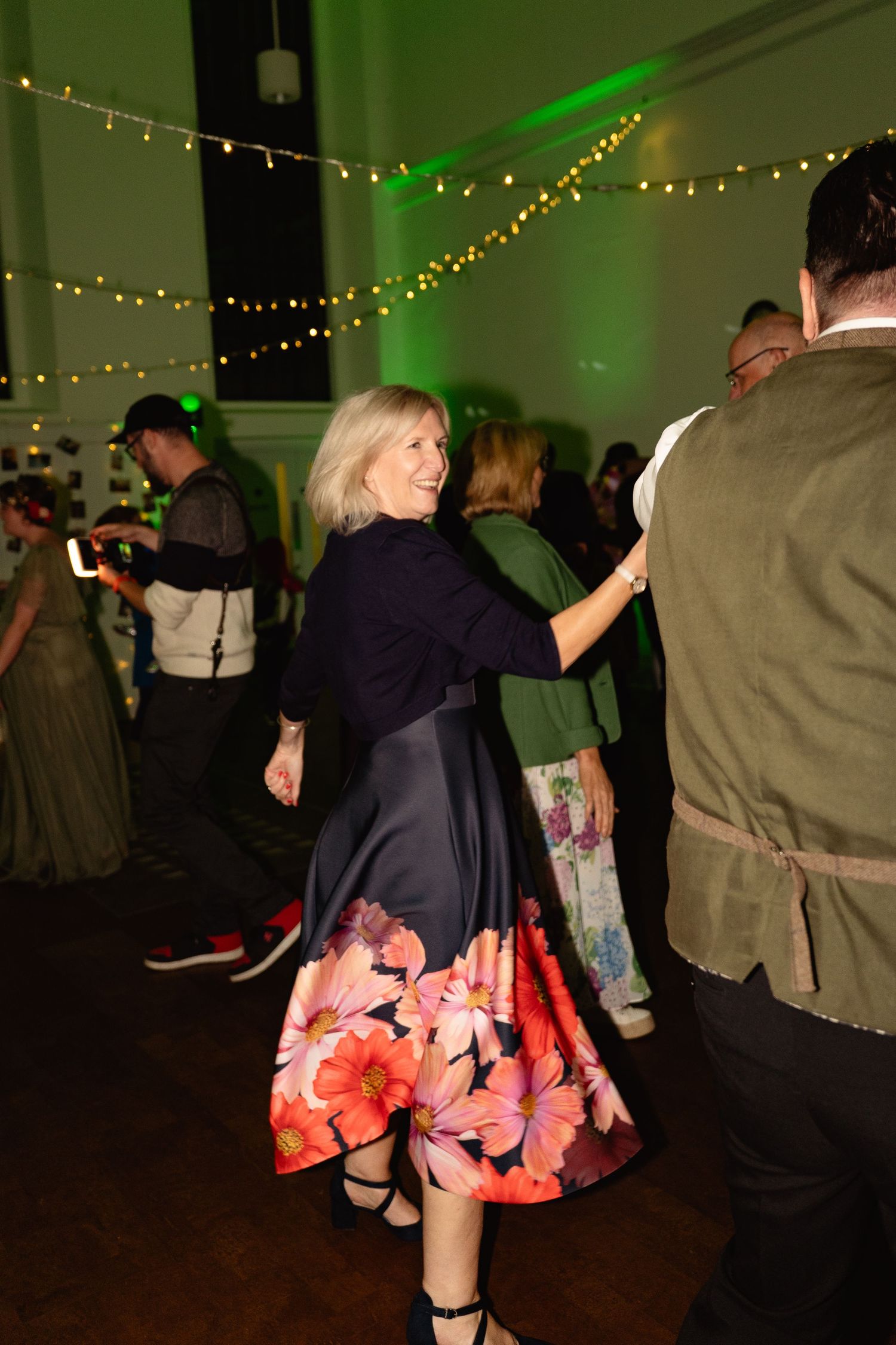 Woman in floral midi skirt dancing at elegant event with string lights and green ambient lighting.