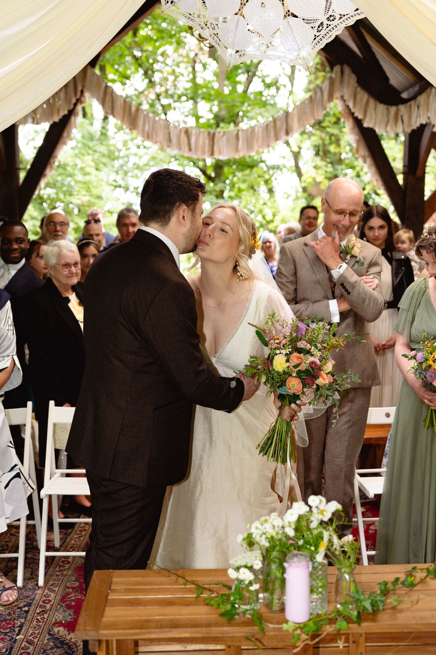Bride and groom share a kiss at the altar during their romantic outdoor woodland wedding ceremony.