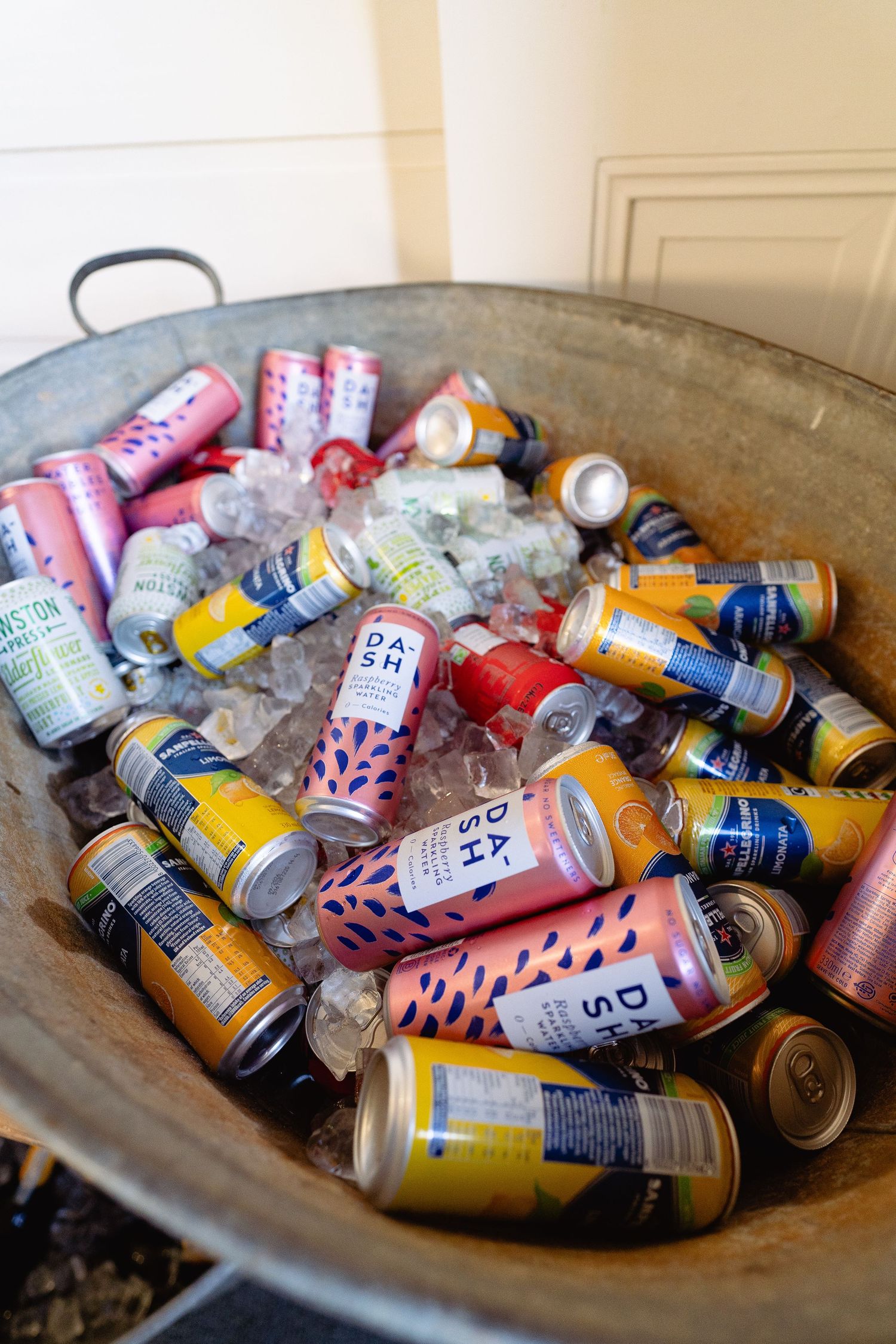 Colorful assorted canned drinks chilling on ice in a large metal tub at an outdoor event.