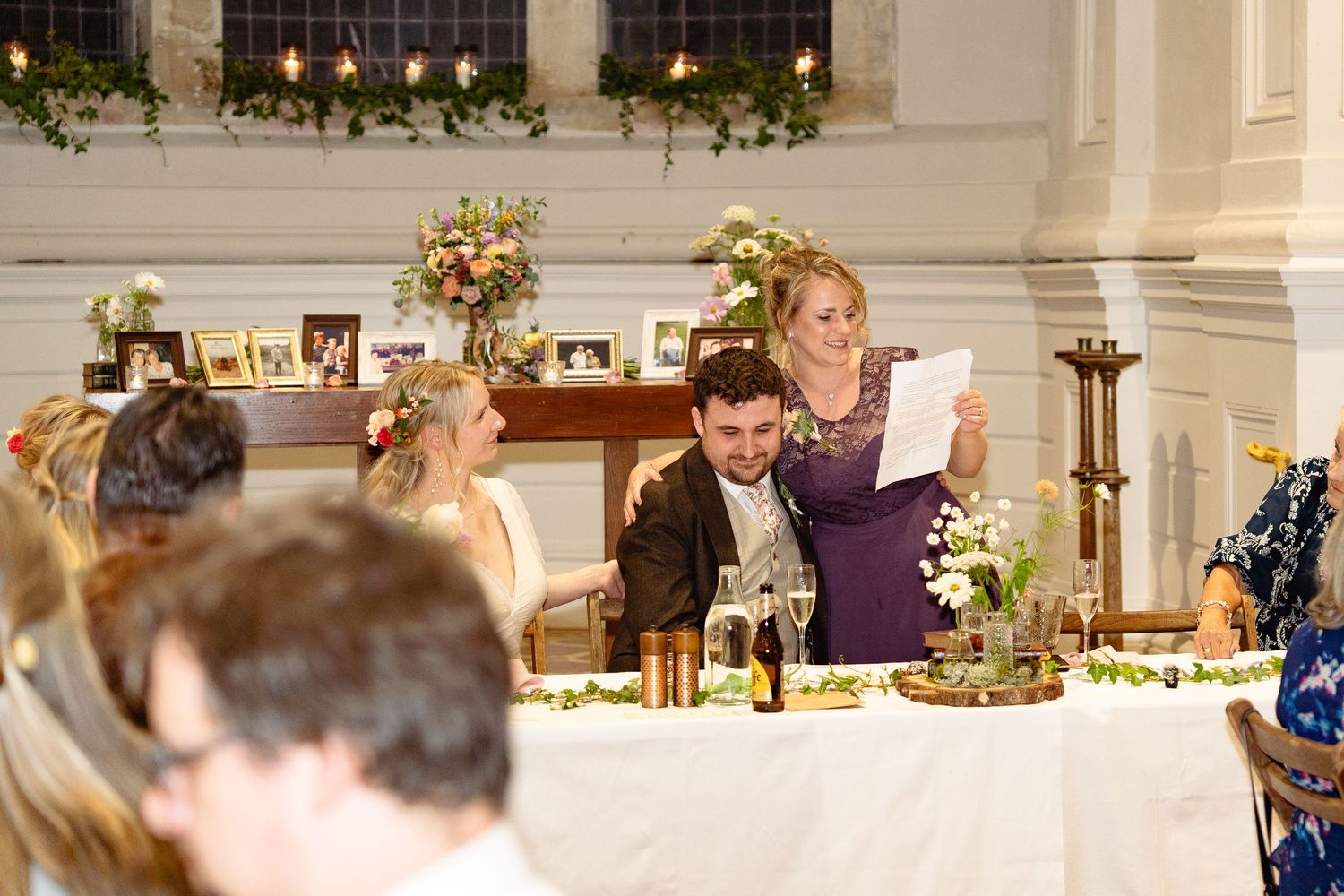 Woman in purple dress gives a toast speech at an elegant wedding reception dinner with floral decorations.