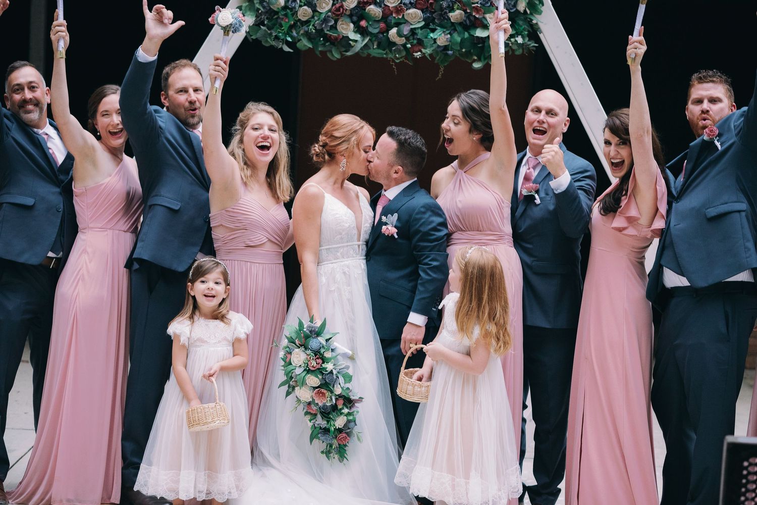 bride and groom kiss while wedding party cheer