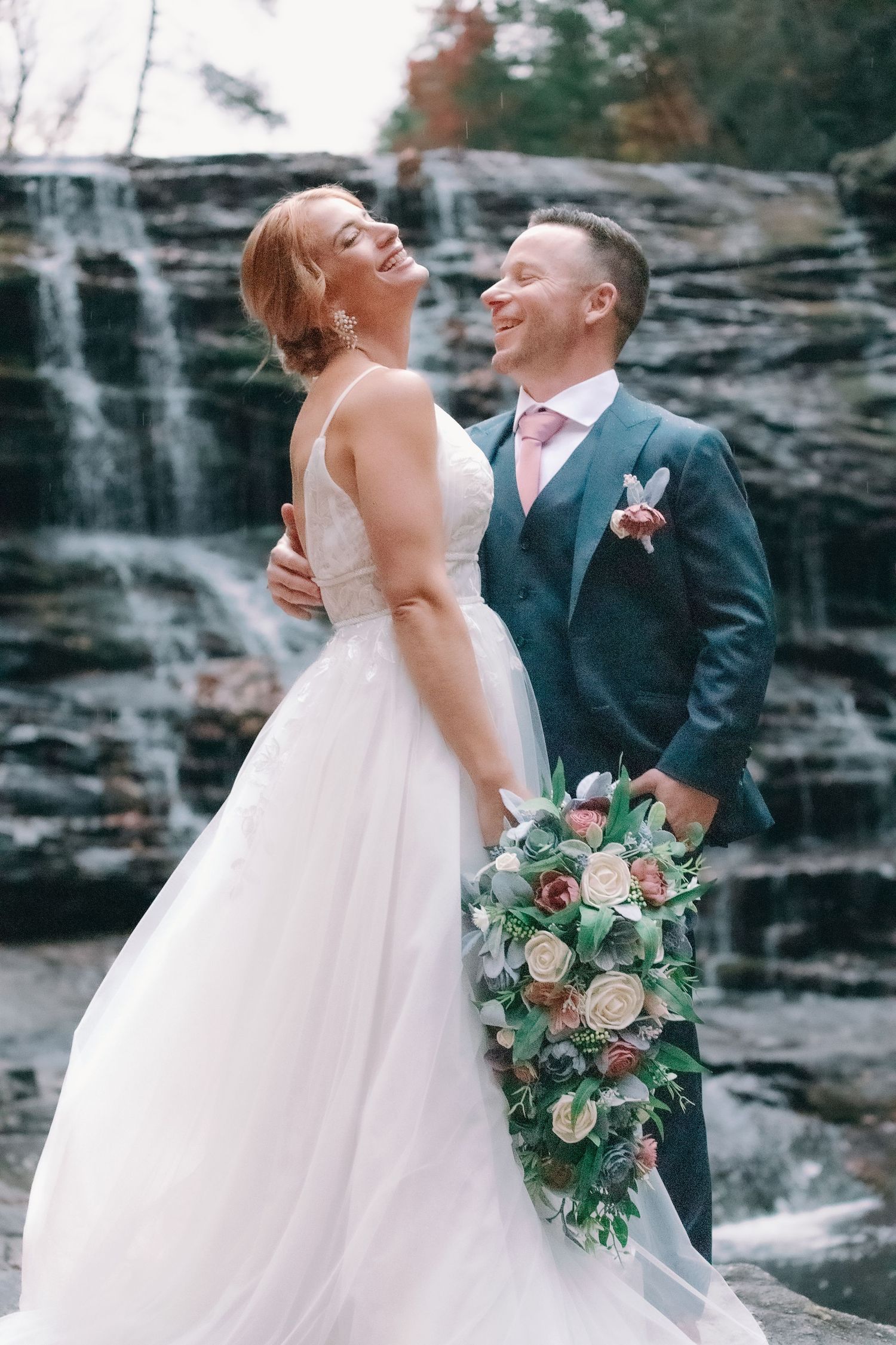 bride laughs in photo of couple in front of waterfall