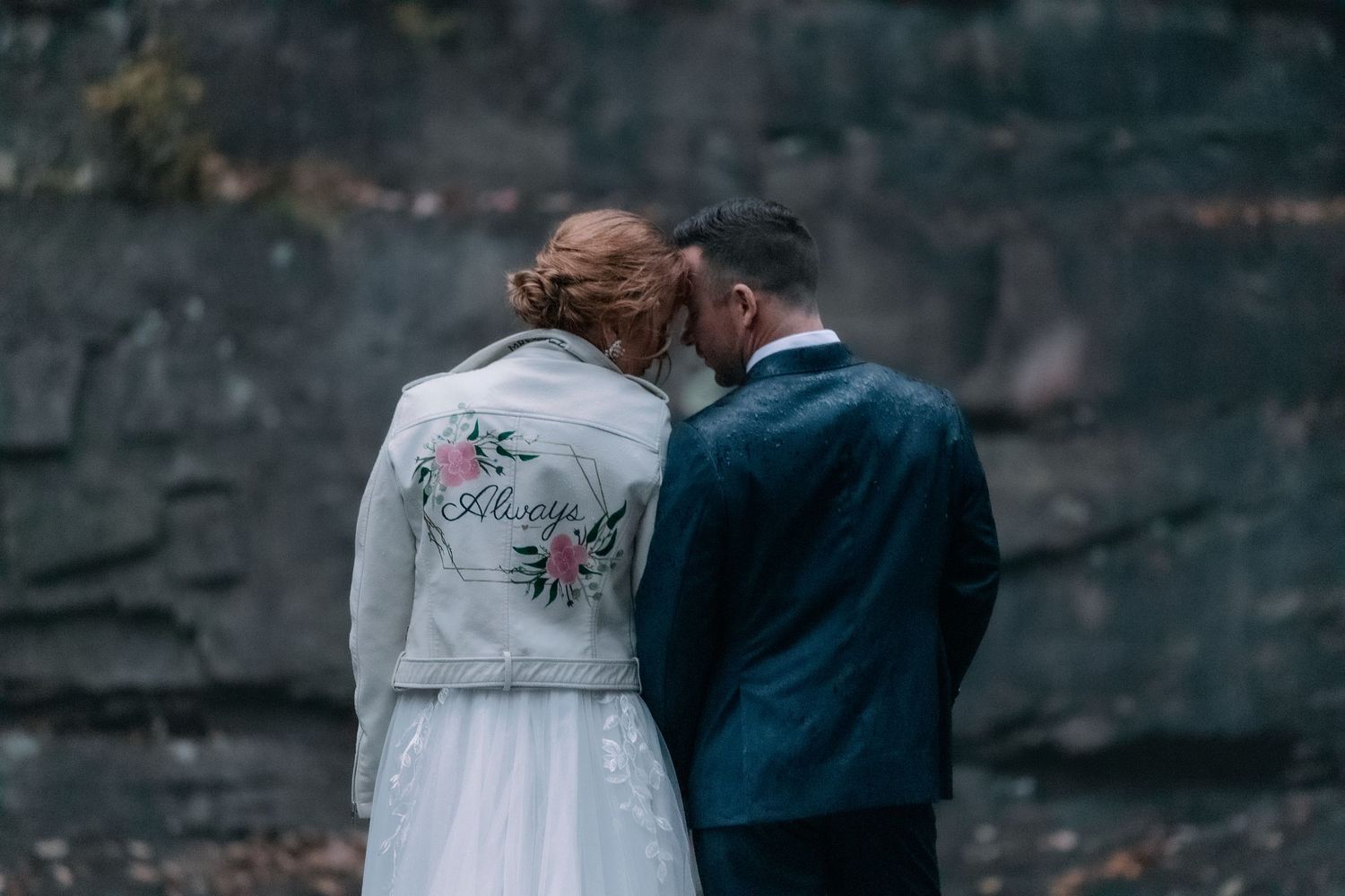 bride and groom stand together leaning their heads together and bride weras demin jacket that says always