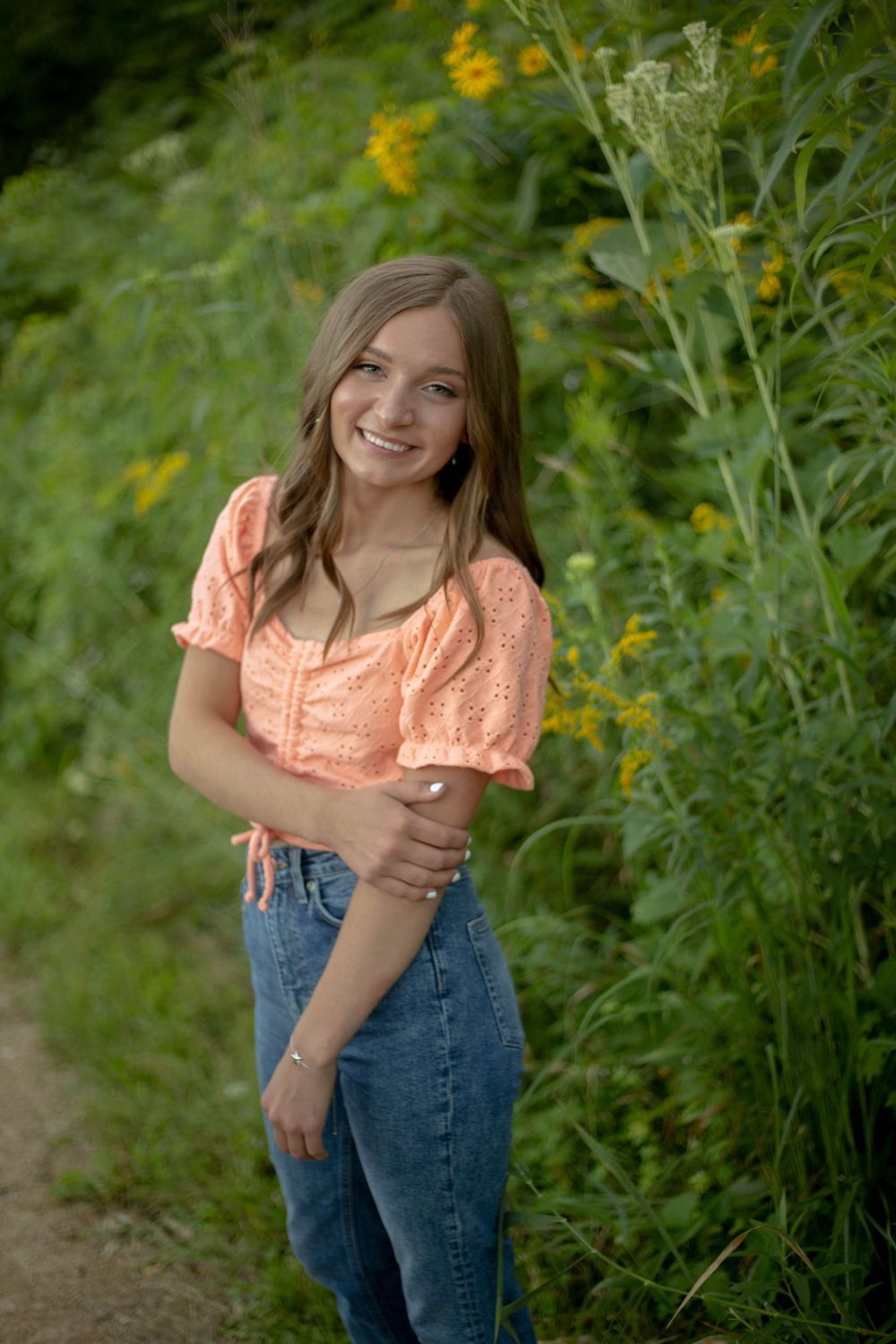 Person wearing peach colored top and jeans poses in field of wildflowers. Mauston photographer.