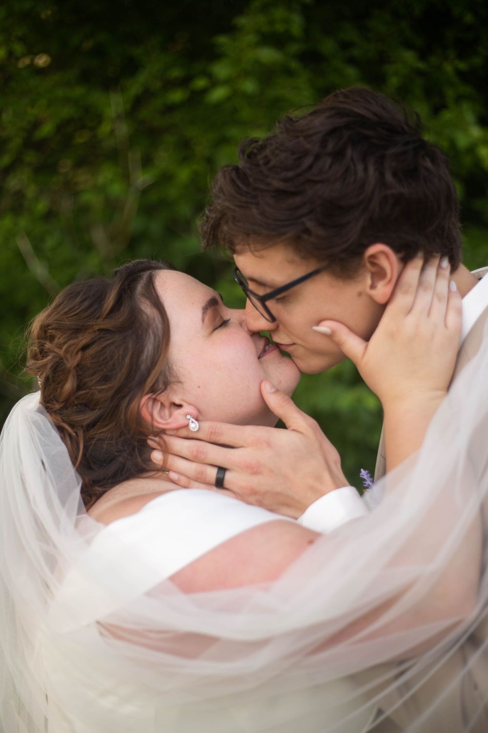 Romantic wedding moment captured through sheer veil in garden setting. Mauston photographer.