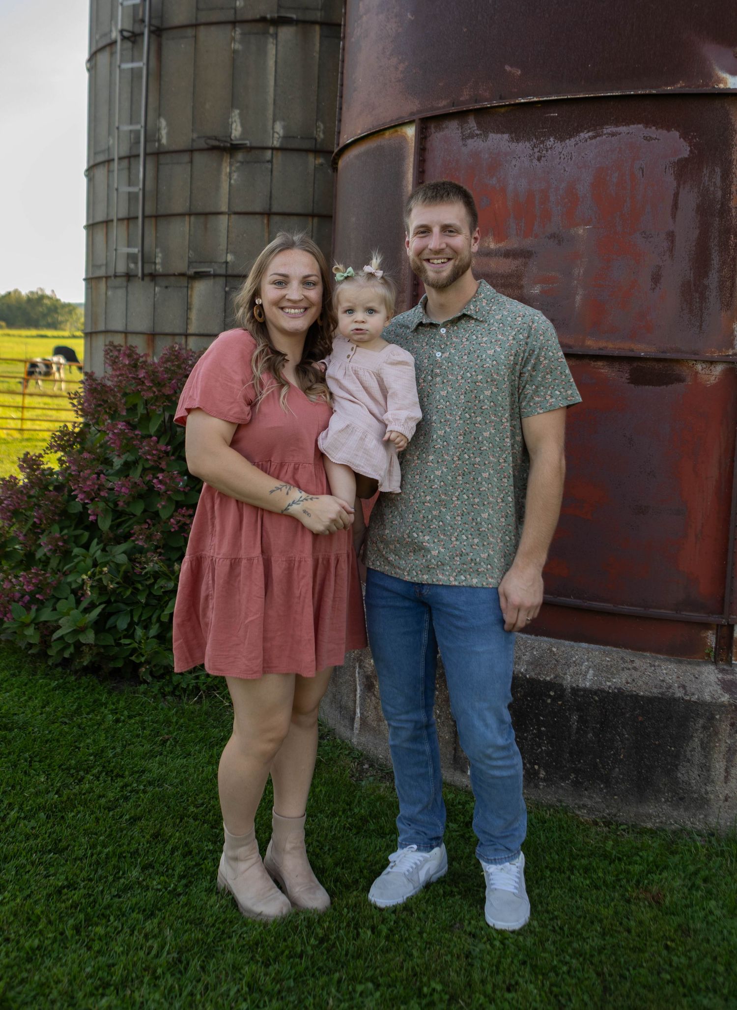 Family portrait against rustic red silo in casual outfits during golden hour. Mauston photographer.