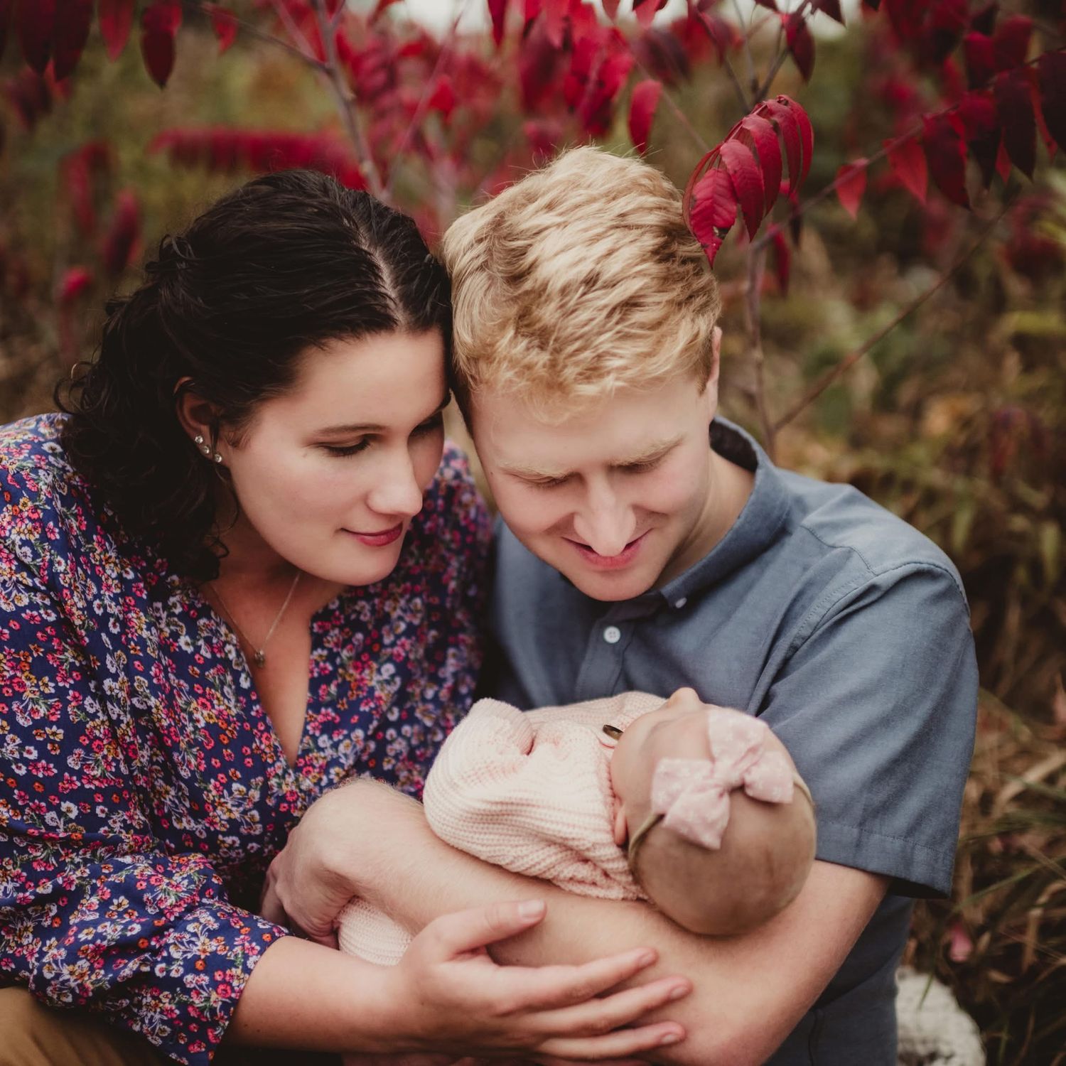Family sharing tender moment with newborn baby among red autumn foliage. Mauston photographer.