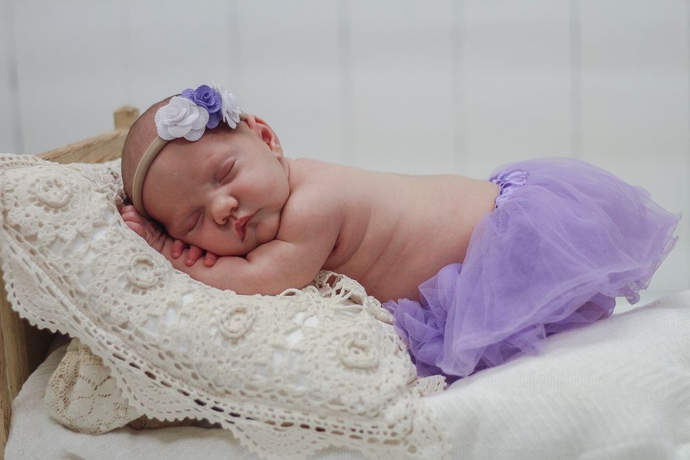 Sleeping baby wearing purple tutu and floral headband on lace pillow. Mauston photographer.