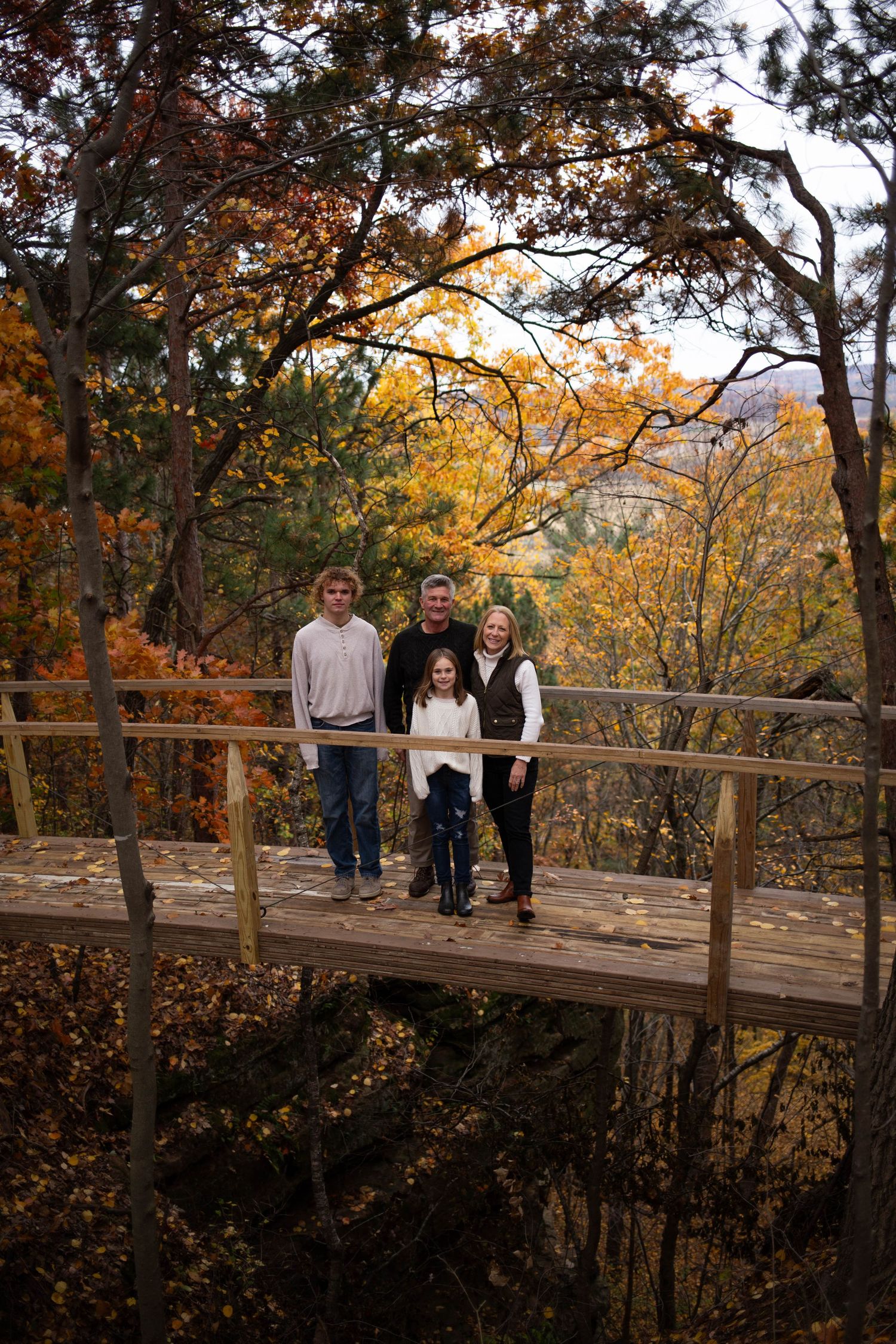 Family group standing on wooden observation deck surrounded by autumn trees. Mauston photographer.