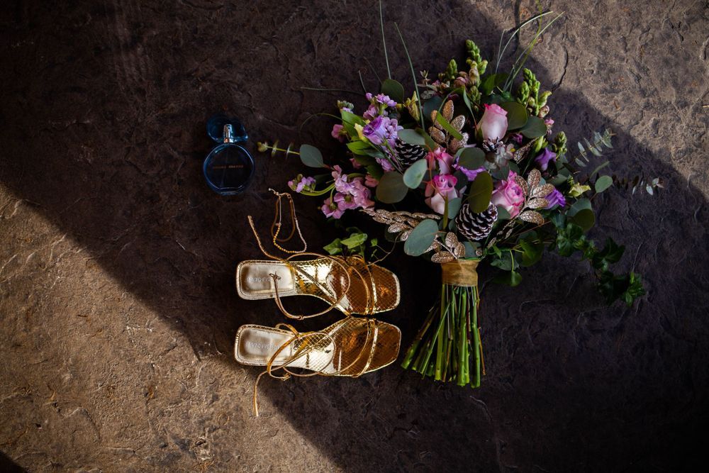 Wedding details flatlay with gold shoes and pink floral bouquet on dark background. Mauston photographer.