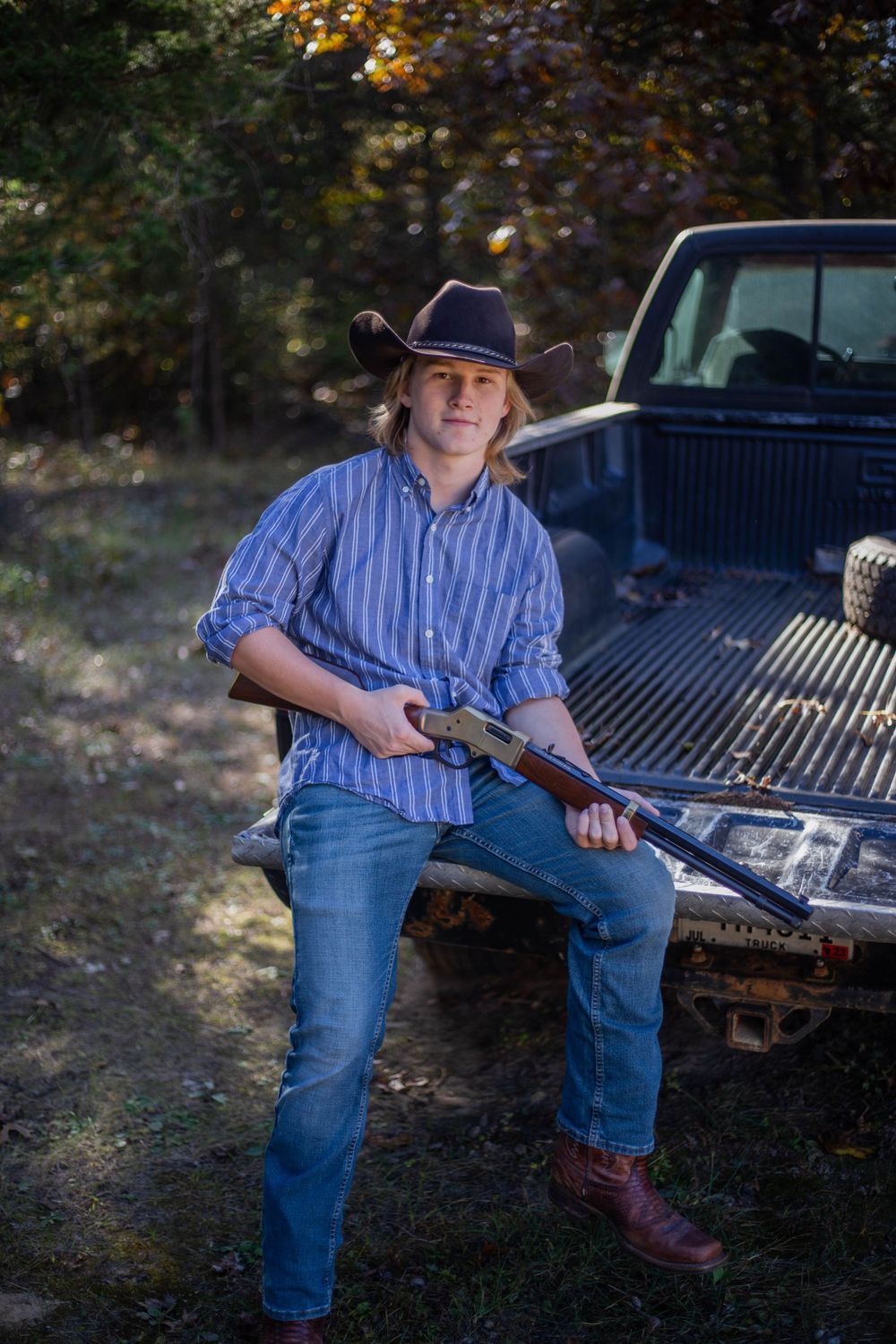Person in striped shirt and jeans sits casually on the back of a pickup truck. Mauston photographer.