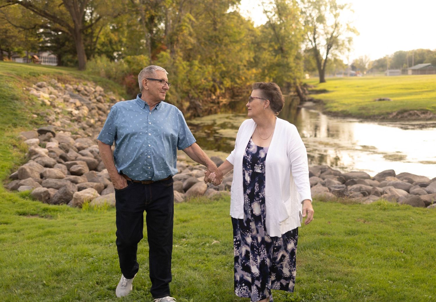 Couple walking together on grassy path near rocky riverbank during autumn. Mauston photographer.
