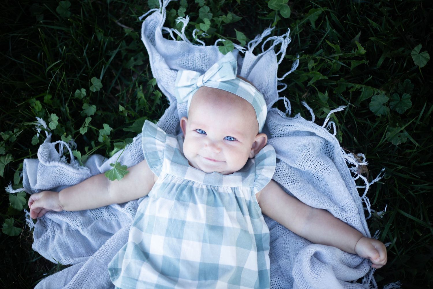 Baby wearing blue and white gingham dress lying on white fabric. Mauston photographer.