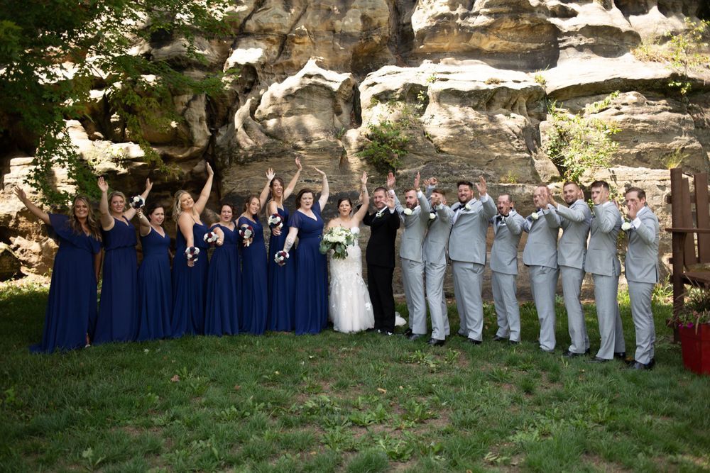 Large wedding party lined up against stone wall wearing navy blue and gray formal attire. Mauston photographer.