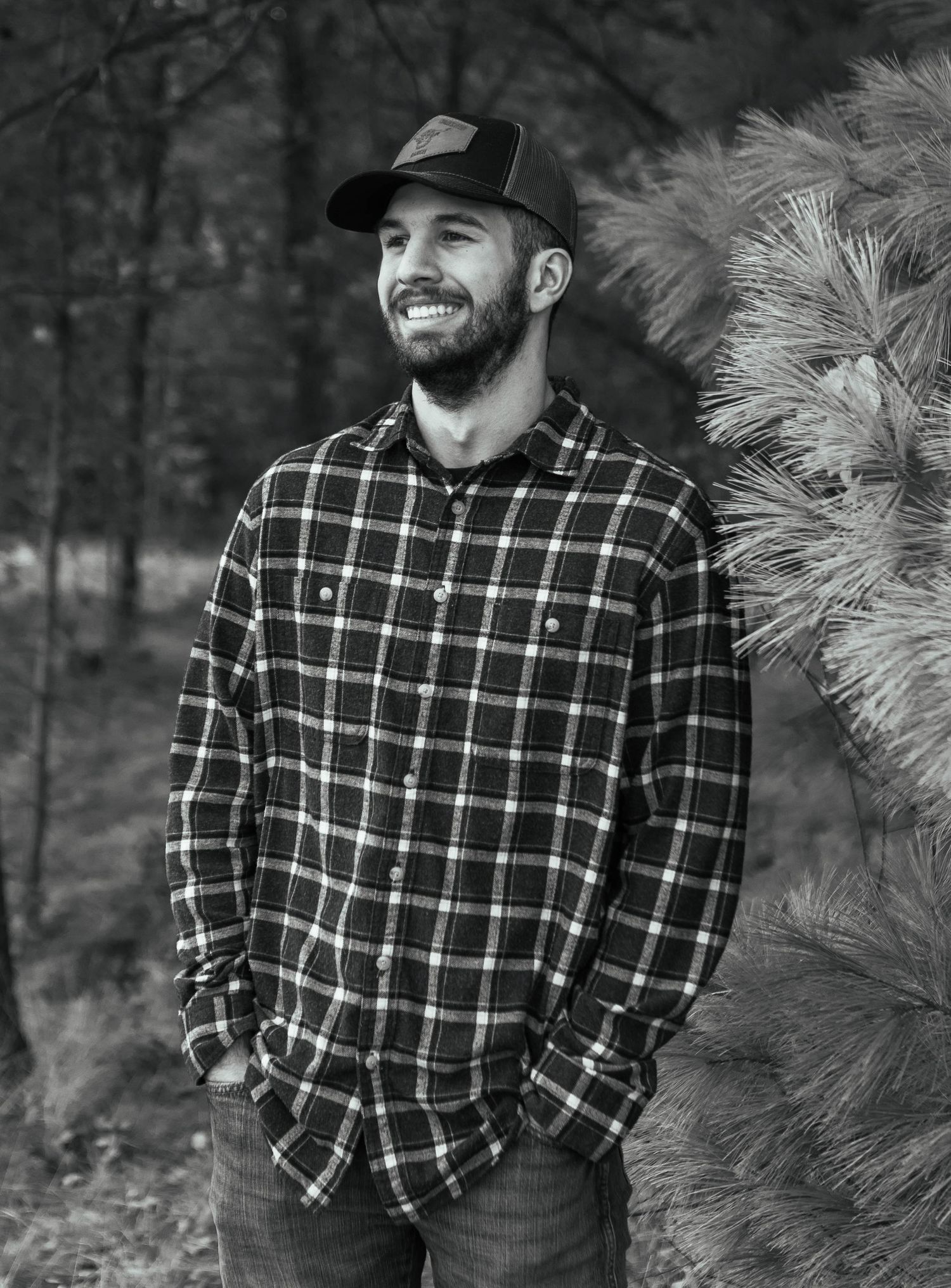Person in plaid flannel jacket poses against dark forest background. Mauston photographer.