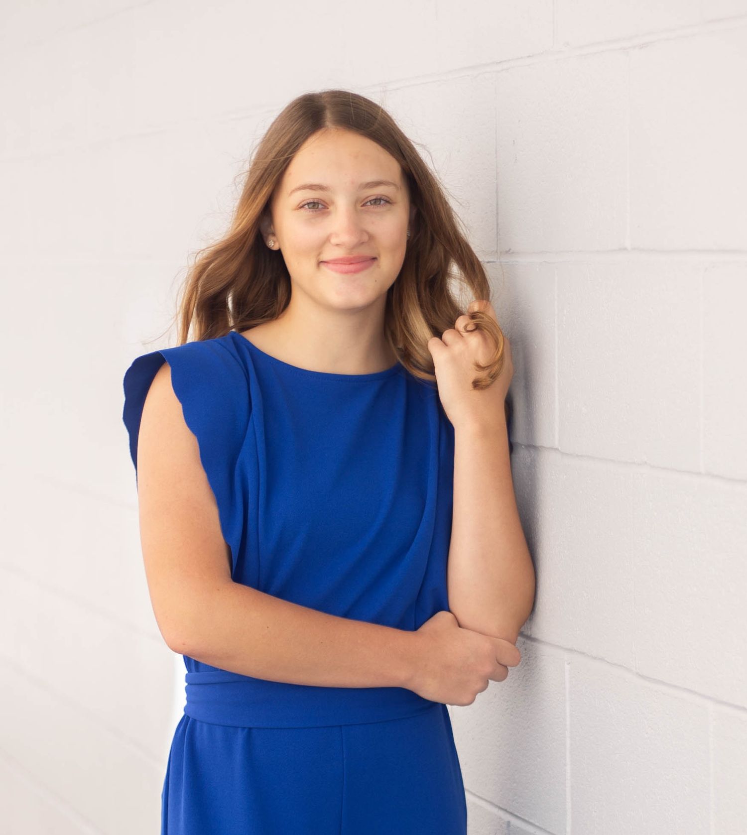 Young woman wearing a royal blue sleeveless dress poses against a white wall in multiple shots. Mauston photographer.