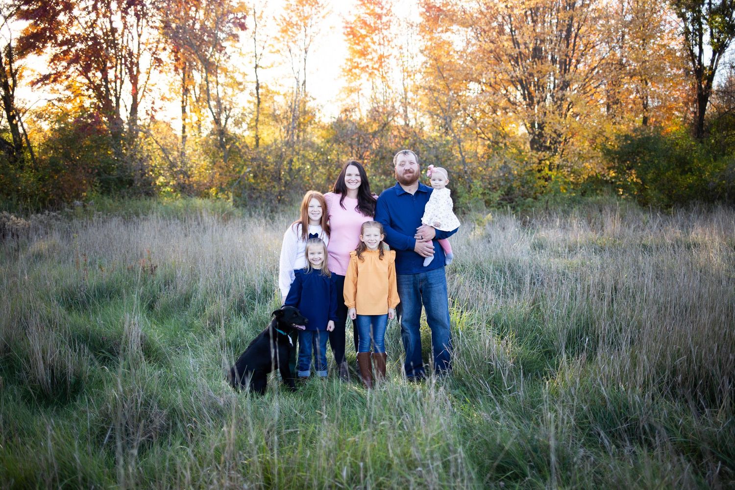 Family gathering in natural meadow setting with golden hour lighting and tall grasses. Mauston photographer.