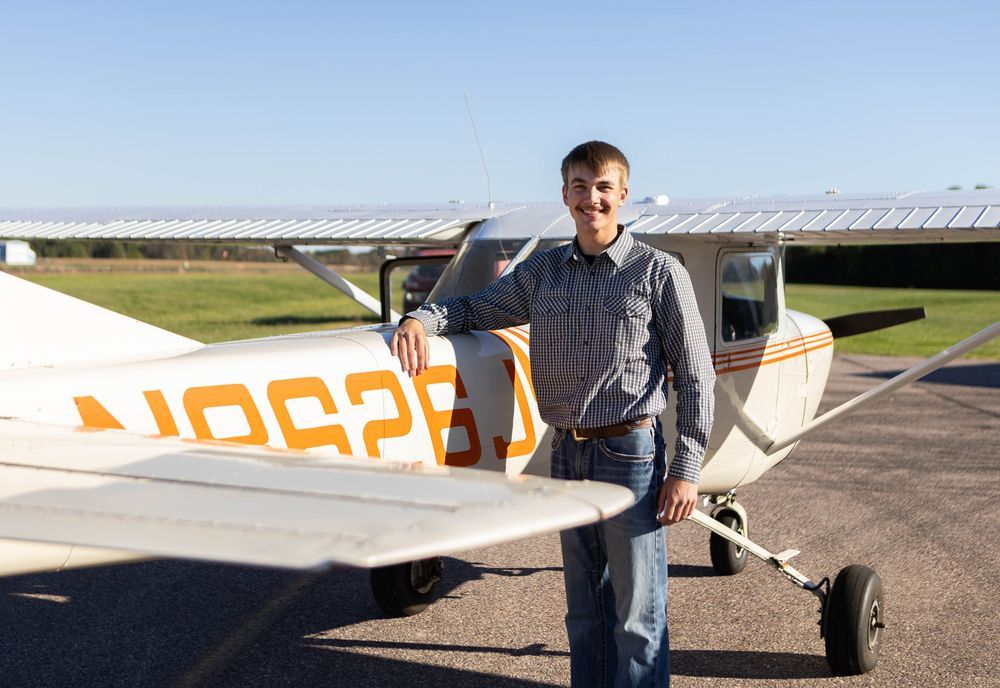 Person stands beside small aircraft on sunny airfield tarmac. Mauston photographer.