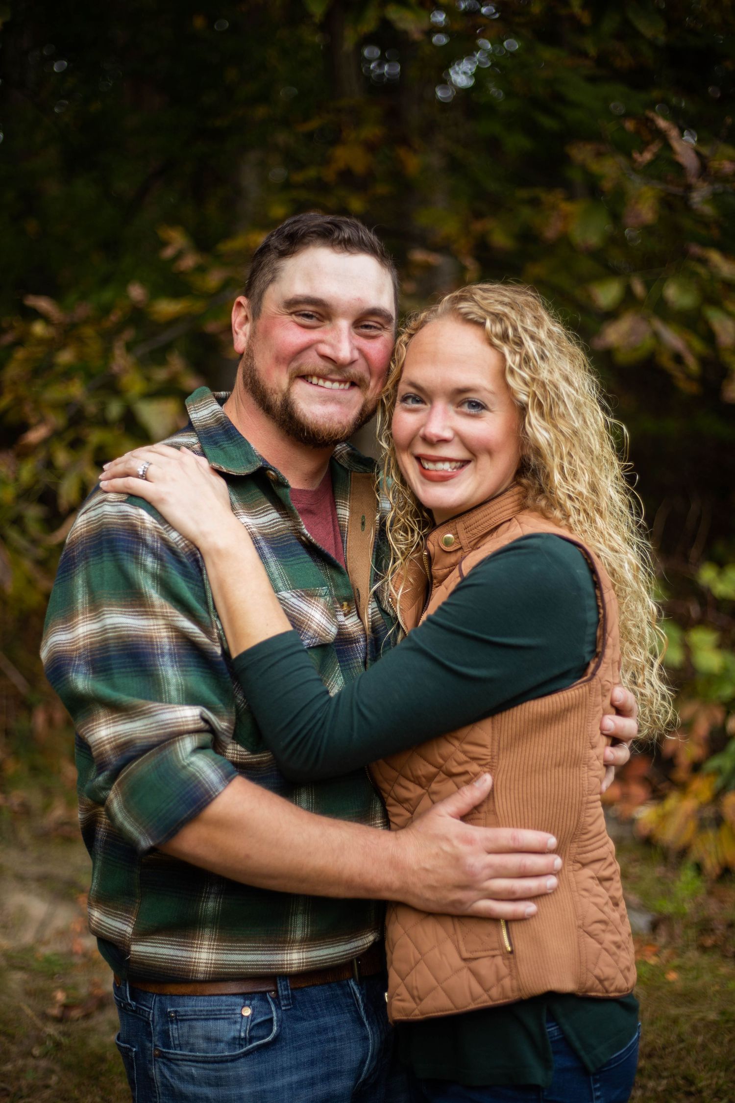 Romantic couple embracing outdoors wearing casual fall attire against autumn foliage. Mauston photographer.