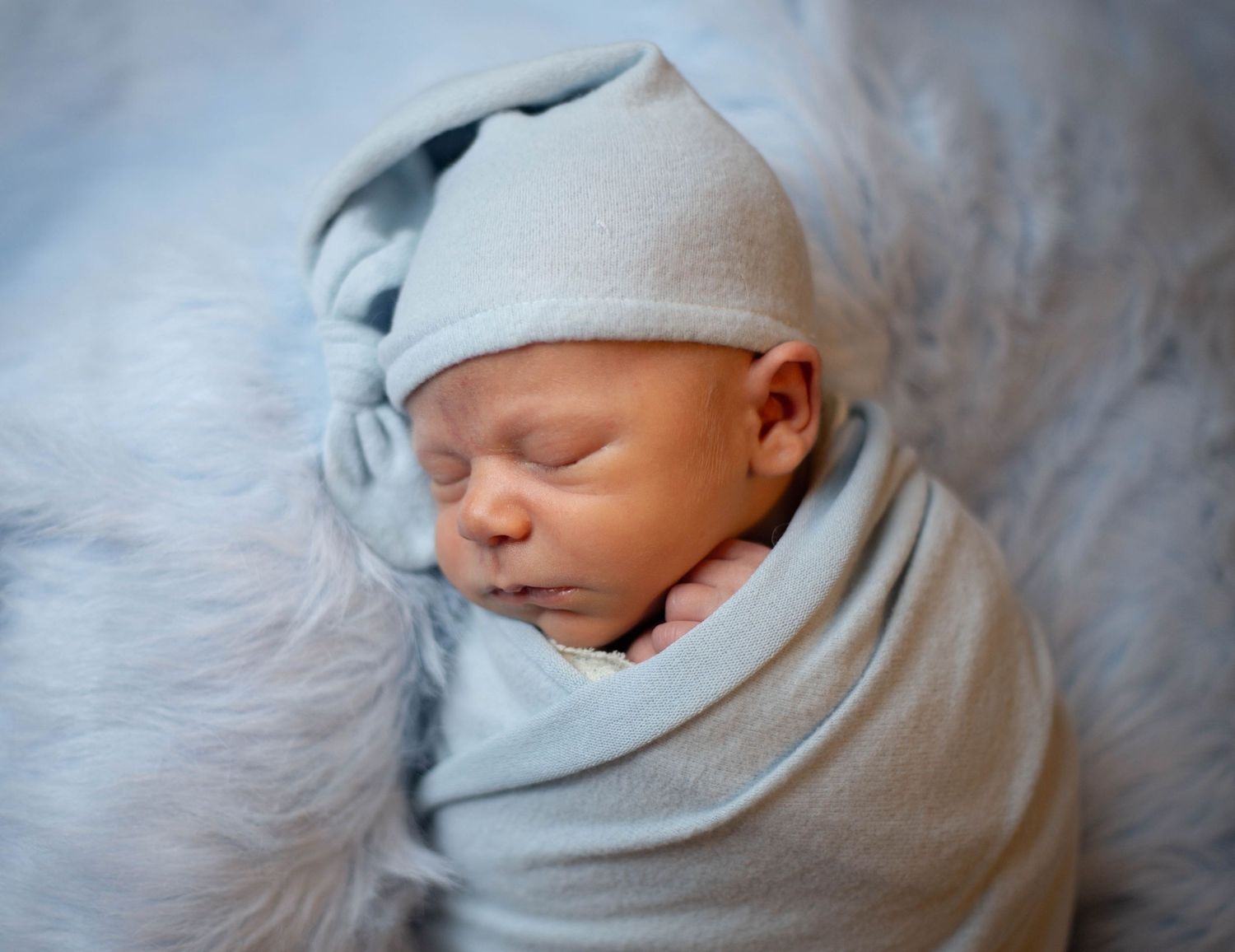 Close-up newborn photography showing baby wrapped in white swaddle against soft gray background. Mauston photographer.