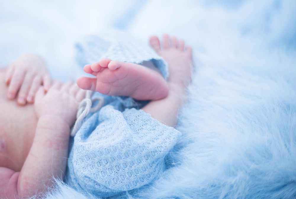 Baby resting on light blue textured blanket with soft lighting and delicate details. Mauston photographer.