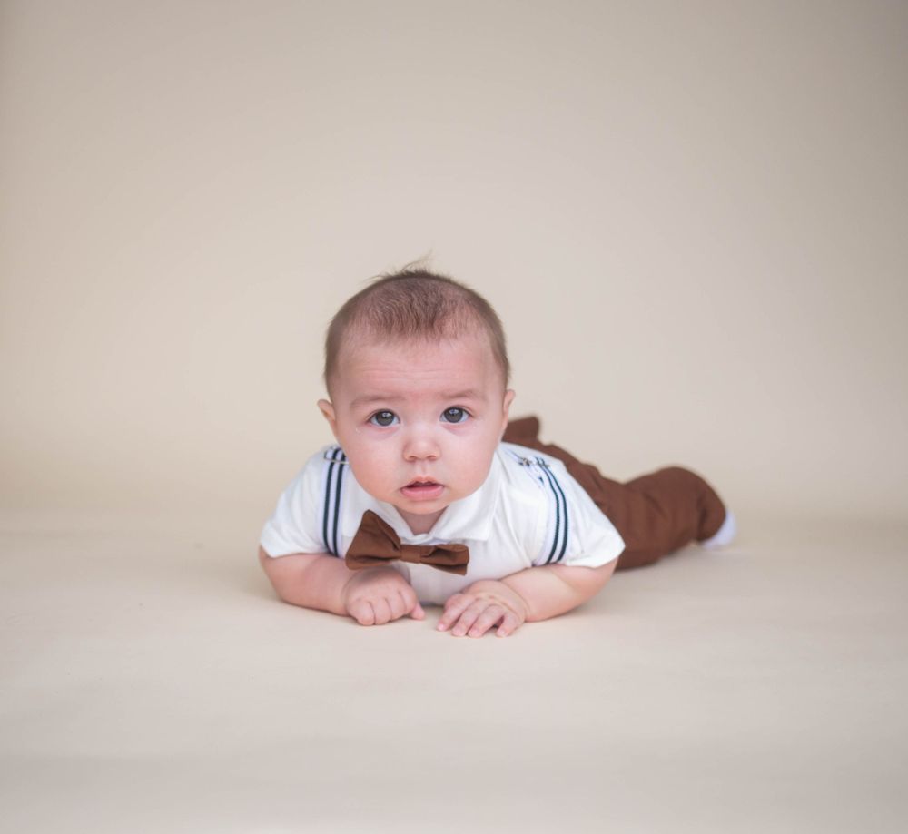 Baby lying on beige background in white outfit during professional photo session. Mauston photographer.