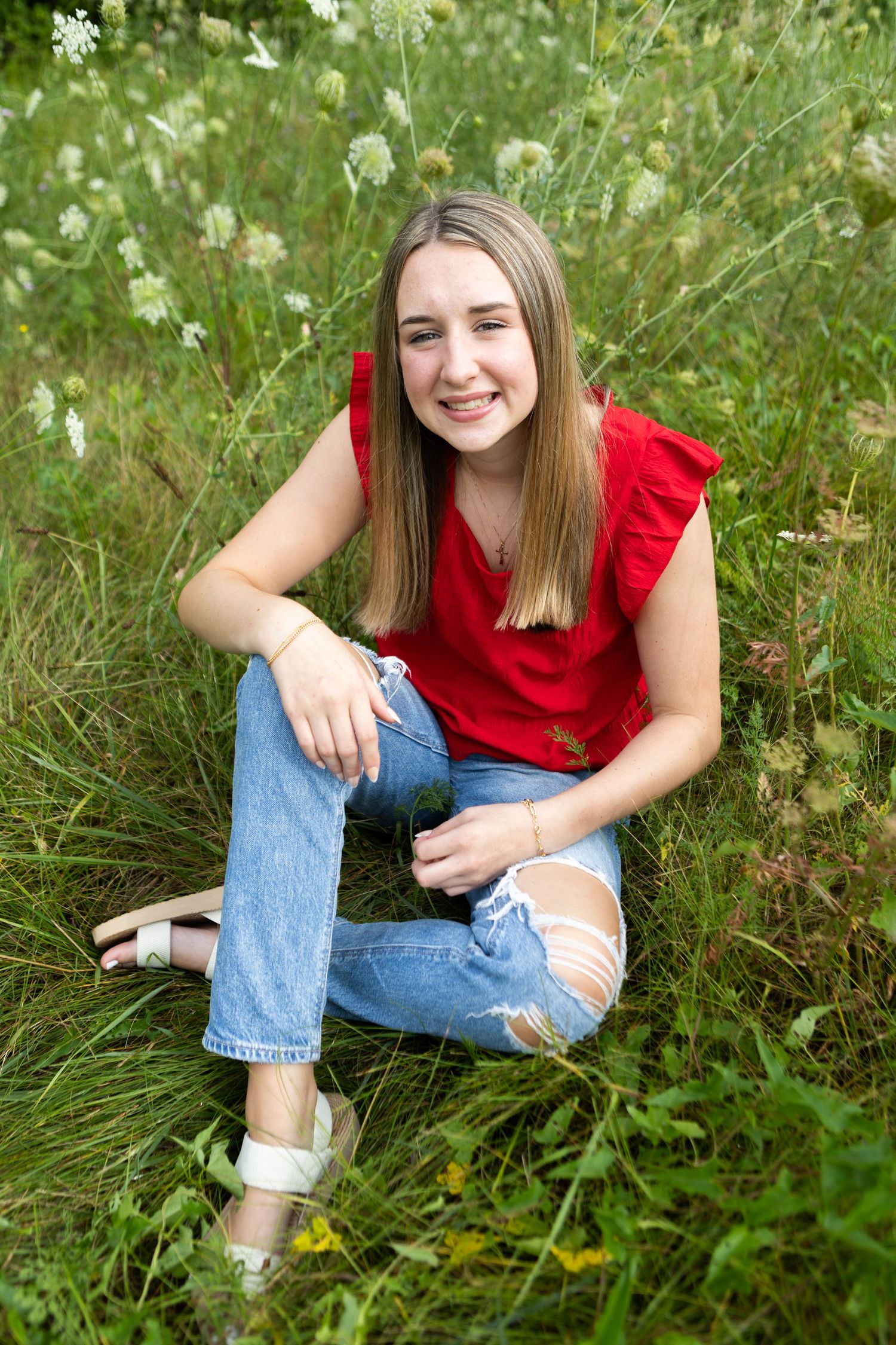 Portrait session in tall grass and wildflowers wearing red top and jeans. Mauston photographer.