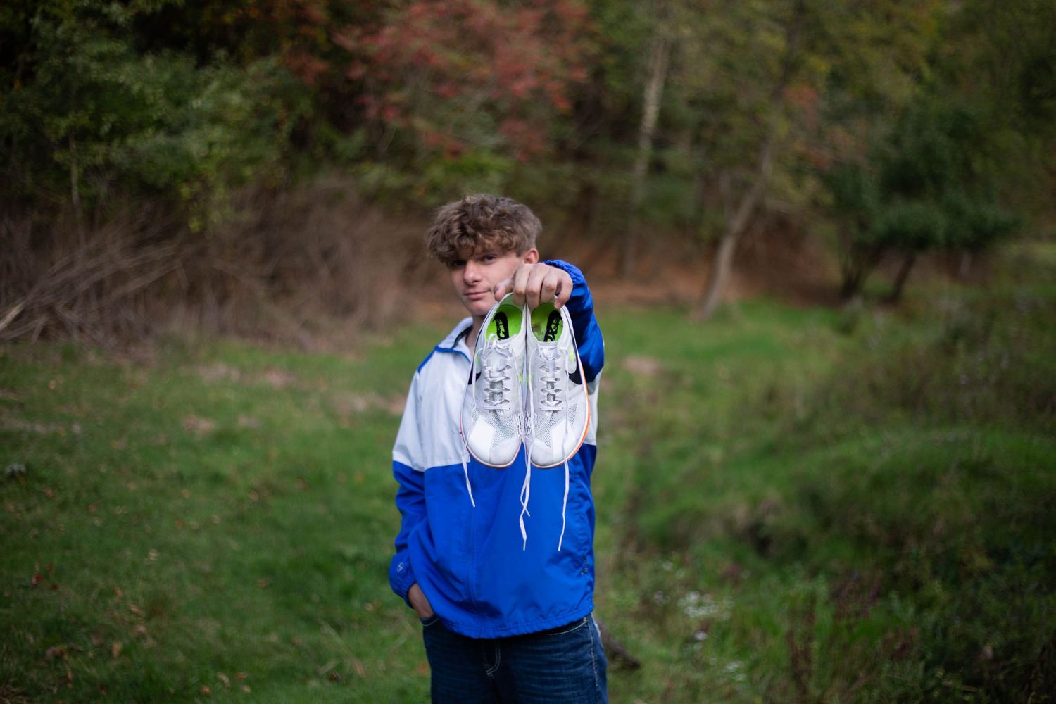 Senior portrait session in a wooded area wearing blue and white athletic jacket. Mauston photographer.