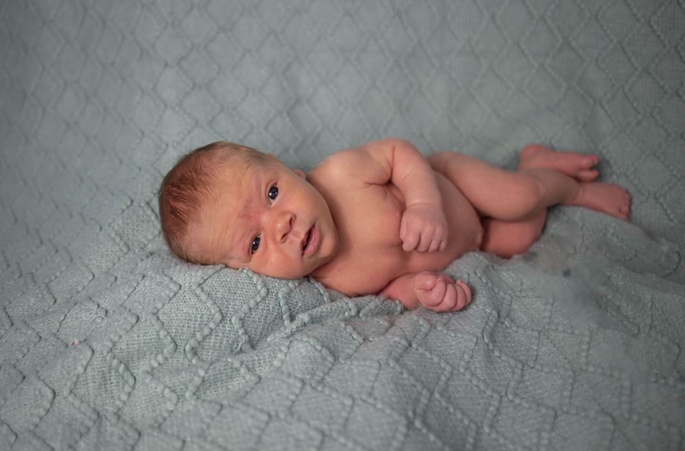 Artistic newborn photography on gray textured blanket showing natural poses. Mauston photographer.