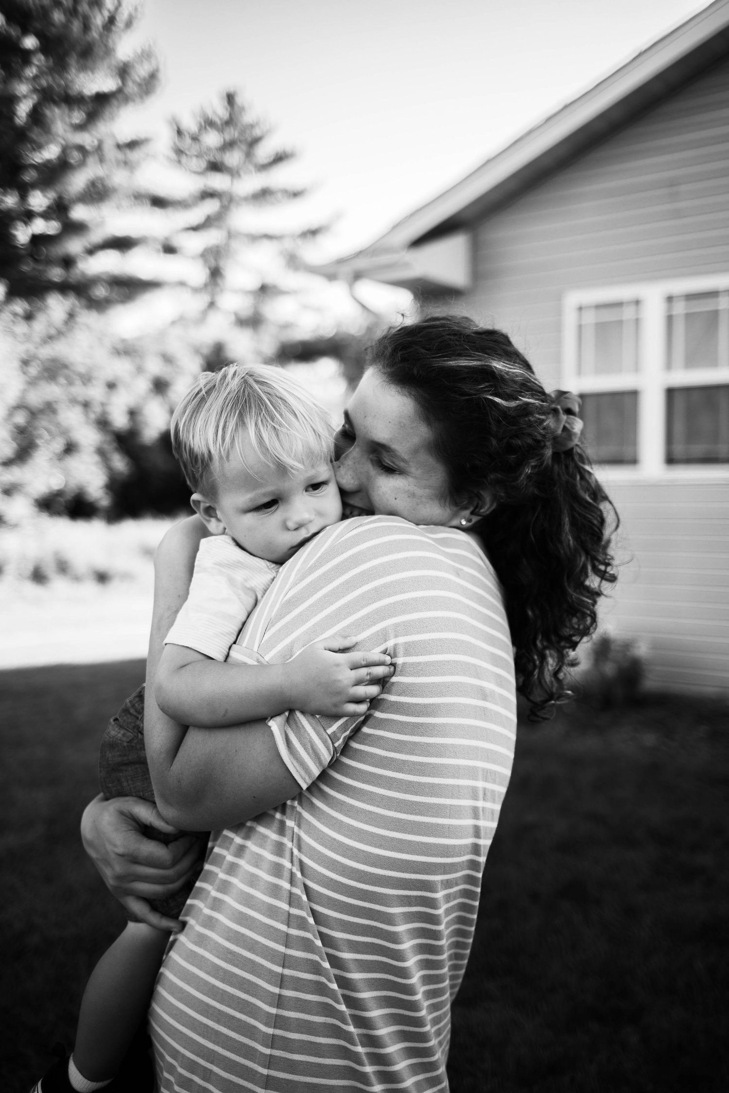 Intimate black and white portrait of tender embrace against house exterior. Mauston photographer.