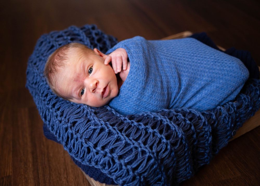 Sleeping newborn wrapped in blue blanket on dark wooden surface. Mauston photographer.