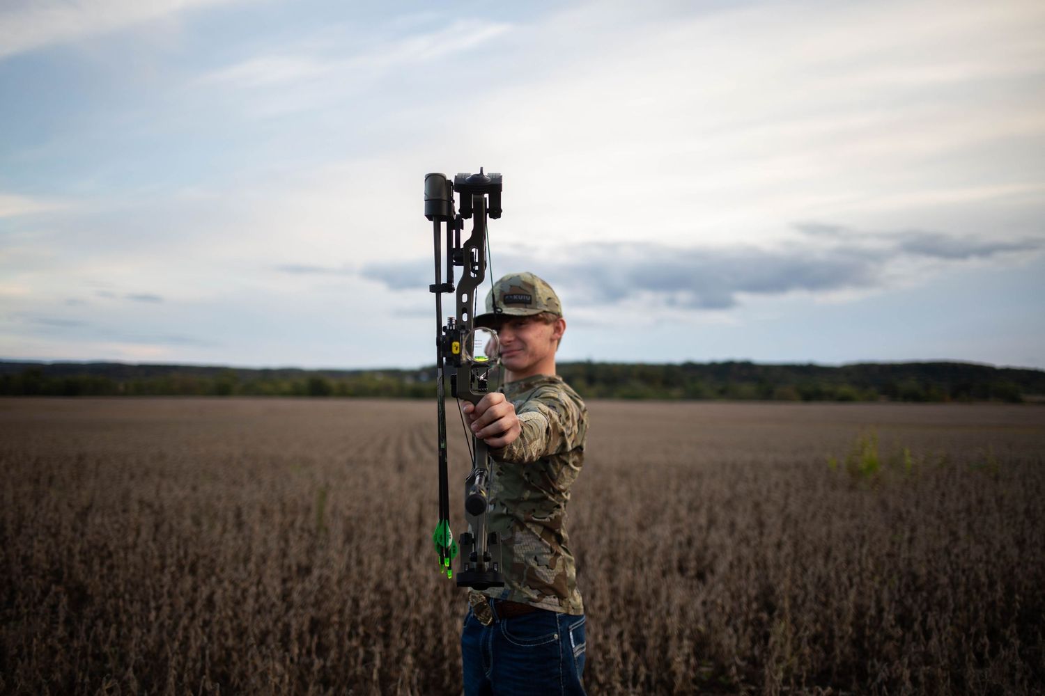 Hunter in camouflage gear aiming a bow in an autumn field. Mauston photographer.
