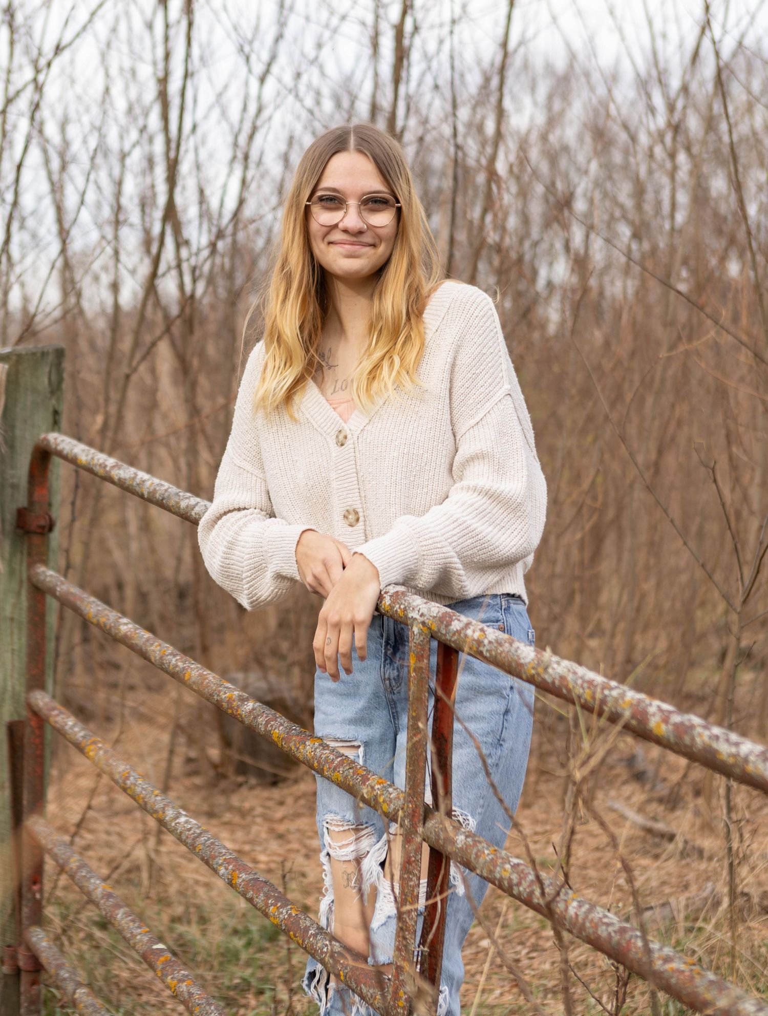 Person in casual sweater and jeans poses by rustic wooden fence in winter landscape. Mauston photographer.