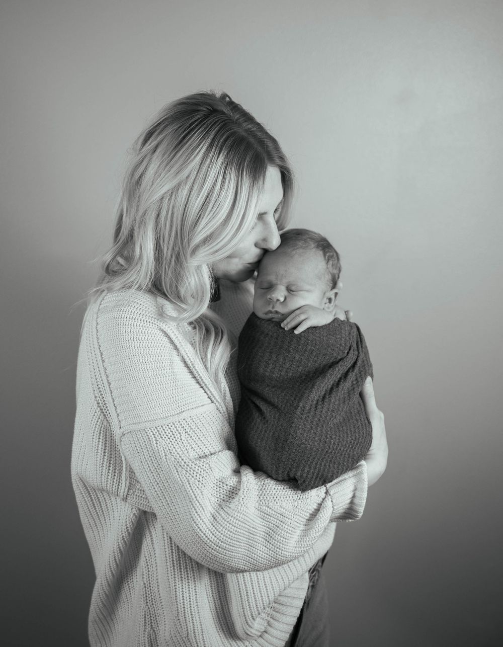 Tender moment captured in black and white as parent holds sleeping baby in knit sweater. Mauston photographer.