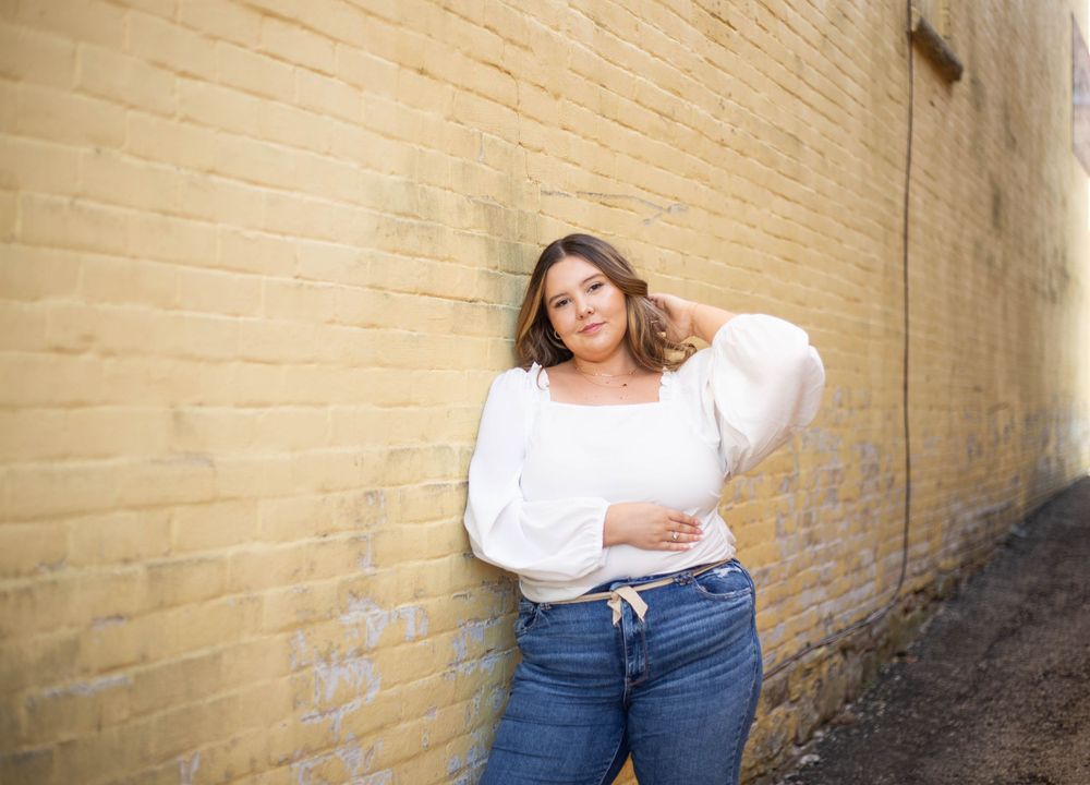 Person in casual outfit leaning against textured beige brick wall. Mauston photographer.