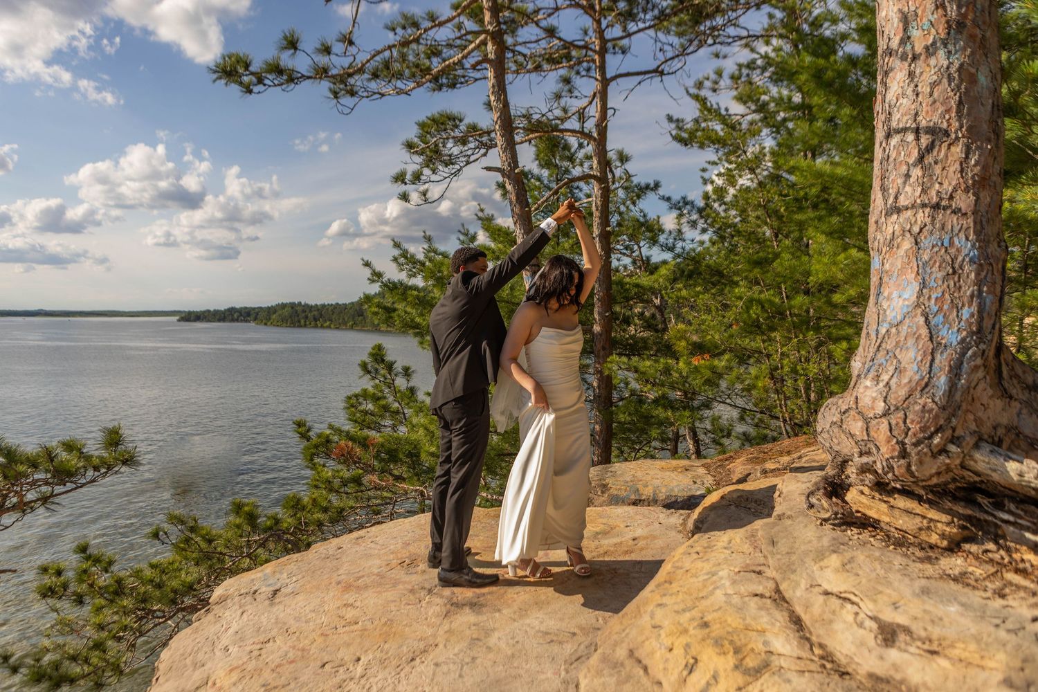 Couple dancing on rocky overlook with pine trees and lake views on their wedding day.