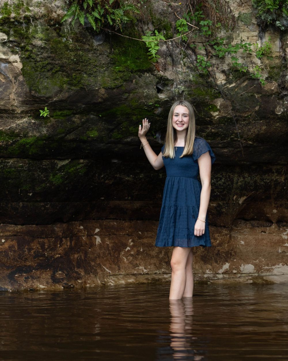 Person in blue dress stands in shallow water against rocky cliff wall. Mauston photographer.