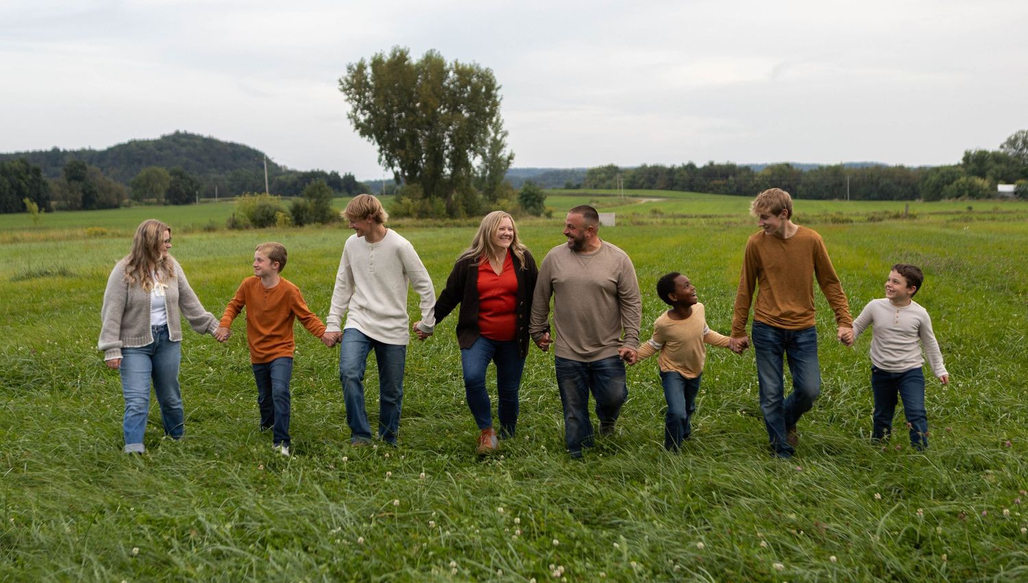Line of people holding hands while standing in a sunny green field. Mauston photographer.