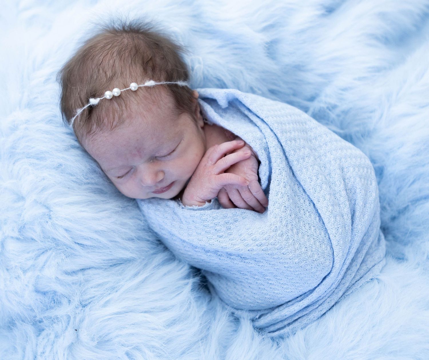 Newborn photography session featuring baby wrapped in soft blue blanket on textured backdrop. Mauston photographer.