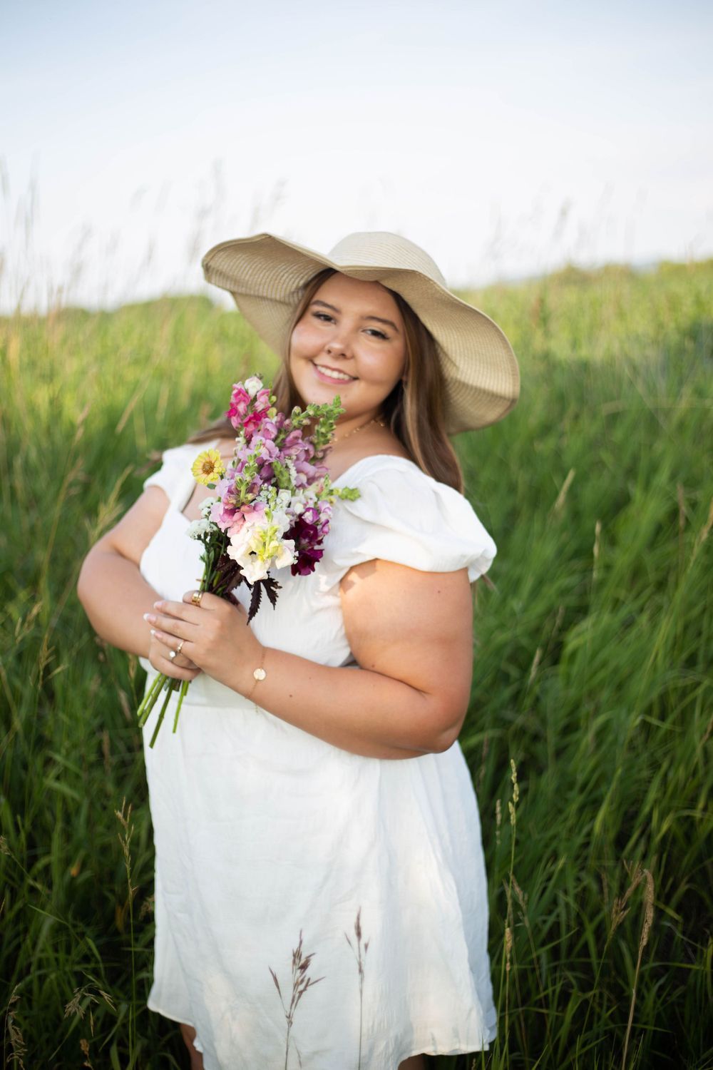 Person in white dress and sun hat holds fresh wildflower bouquet in summer field. Mauston photographer.