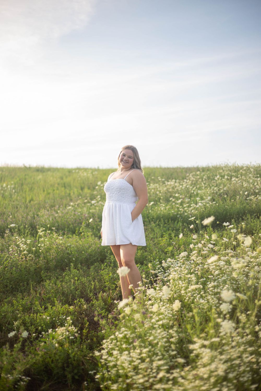 Person in white dress poses gracefully among blooming wildflowers in a sunny meadow. Mauston photographer.