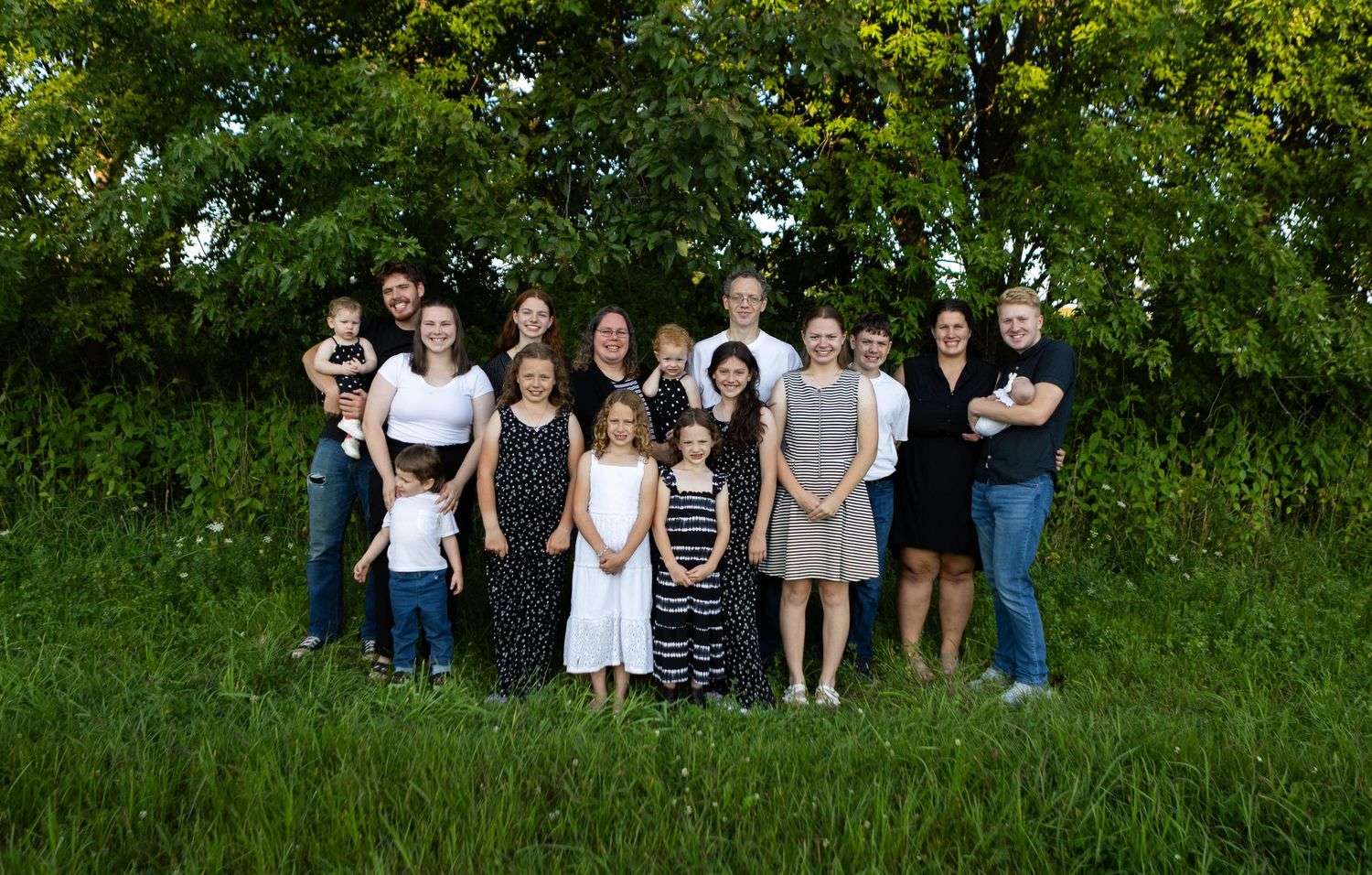 Large family group photo outdoors with green trees and natural backdrop. Mauston photographer.