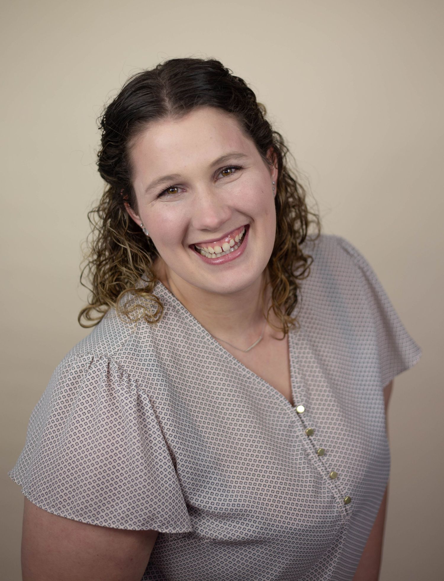 Portrait against neutral beige background wearing polka dot blouse. Mauston photographer.