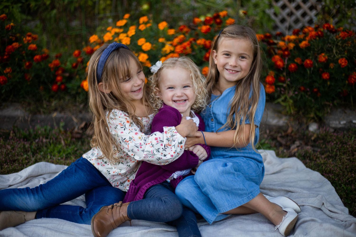 Children playing together on a blanket in a garden with colorful flowers in the background. Mauston photographer.