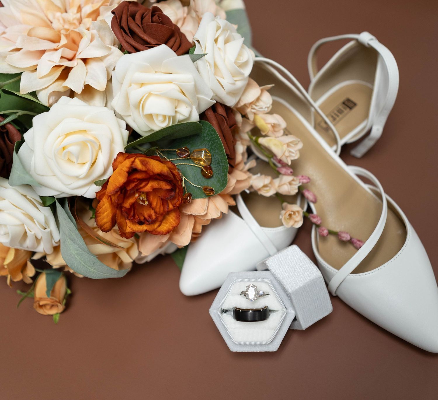 Wedding accessories including peach and white roses, bridal shoes, and jewelry on brown background. Mauston photographer.