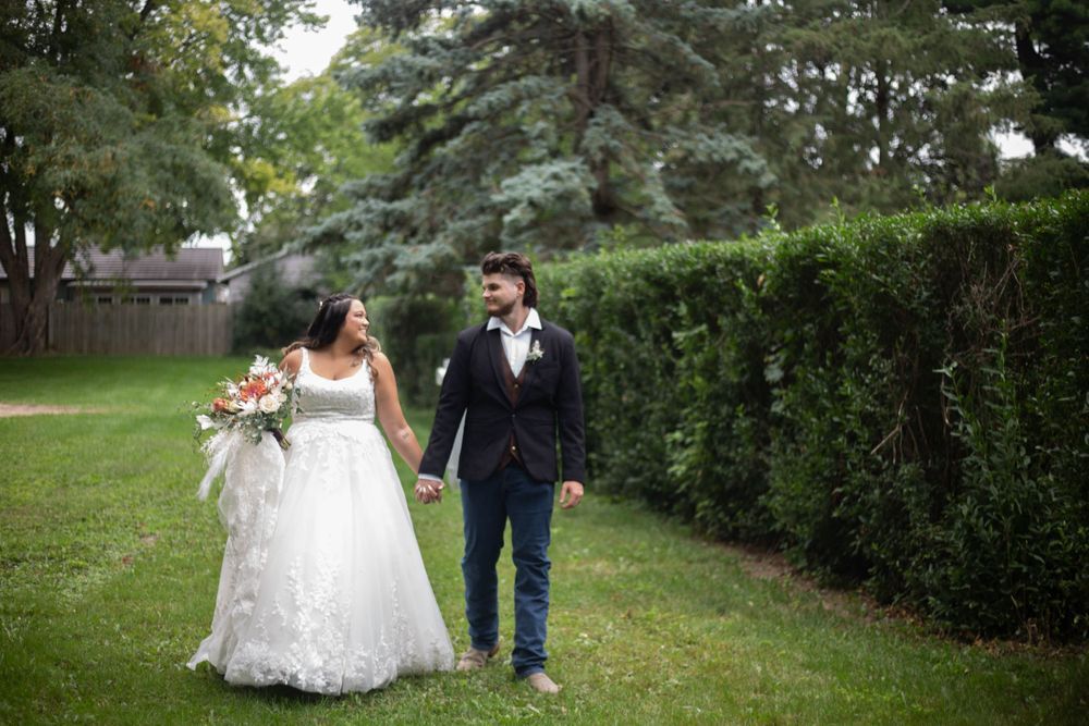 Wedding party in navy blue and gray attire posing outdoors in a garden setting. Mauston photographer.