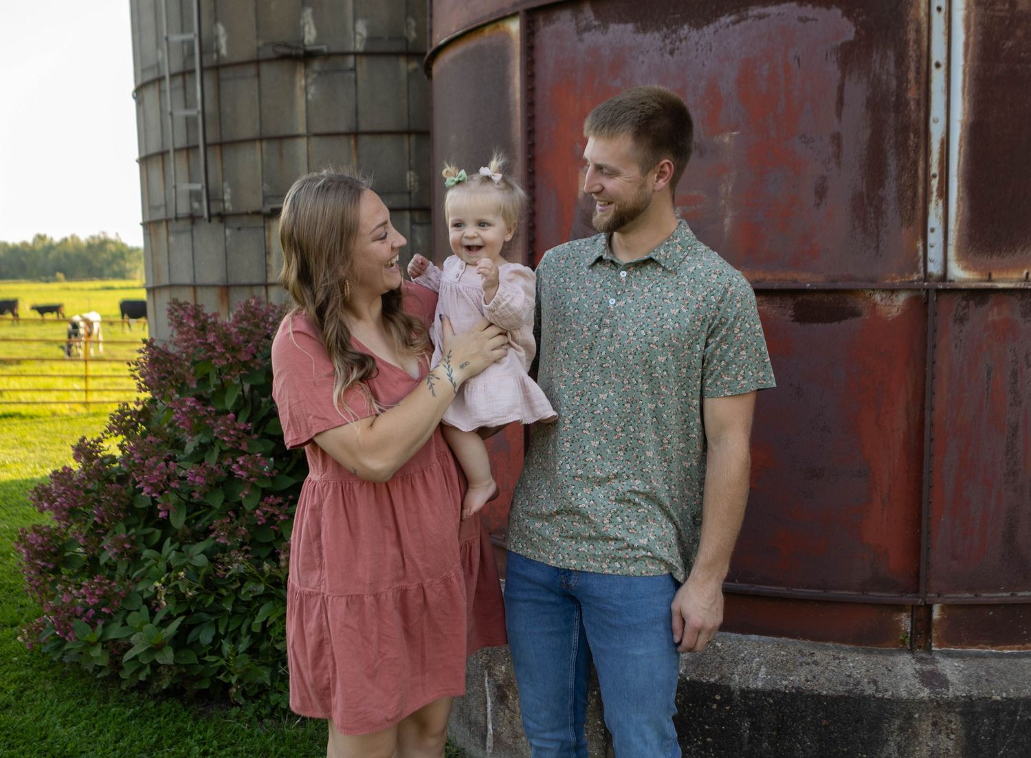 Family poses together in front of a rustic red barn wall during an outdoor photoshoot. Mauston photographer.